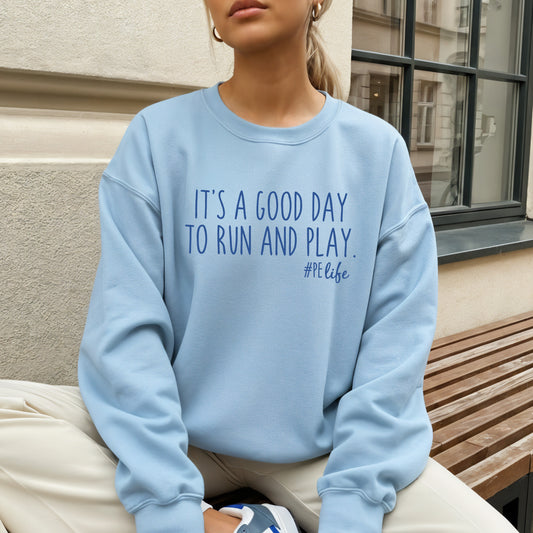 Woman wearing a light blue Gildan sweatshirt that says It's a Good Day to Run and Play #PE life