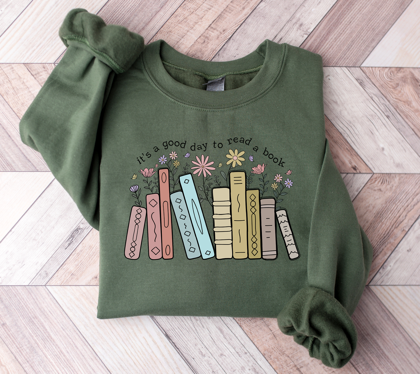 Green sweatshirt with book-themed design on a wooden floor