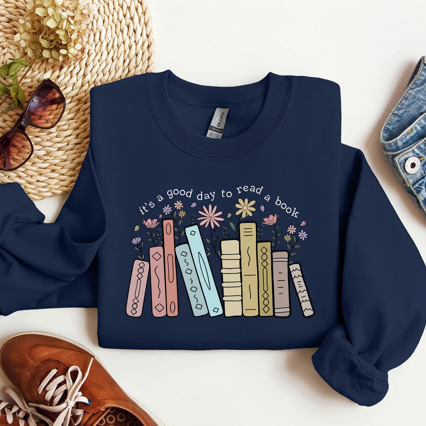 Navy blue sweatshirt with book design and text on a white surface with accessories.