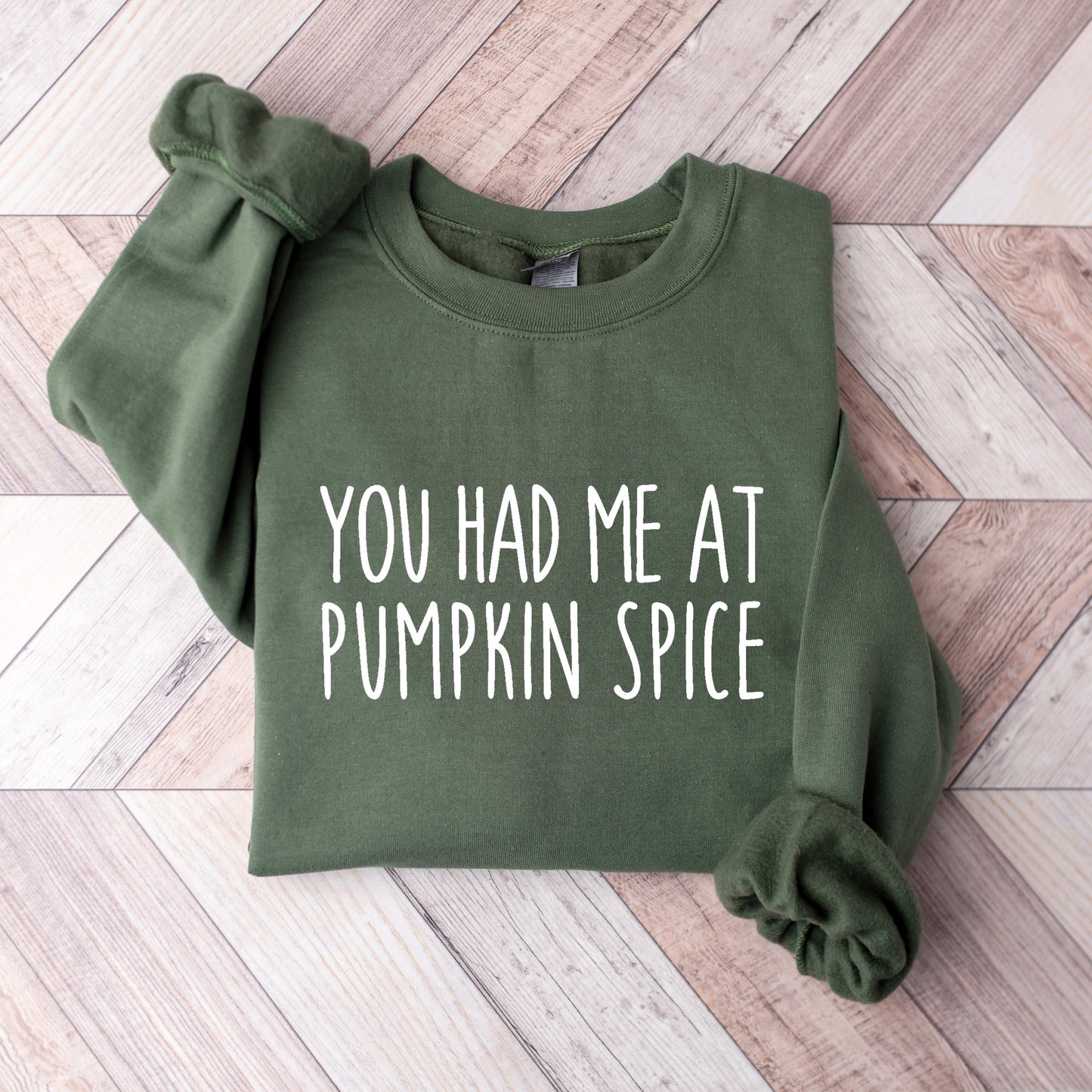 Green sweatshirt with 'You Had Me At Pumpkin Spice' text on a wooden surface
