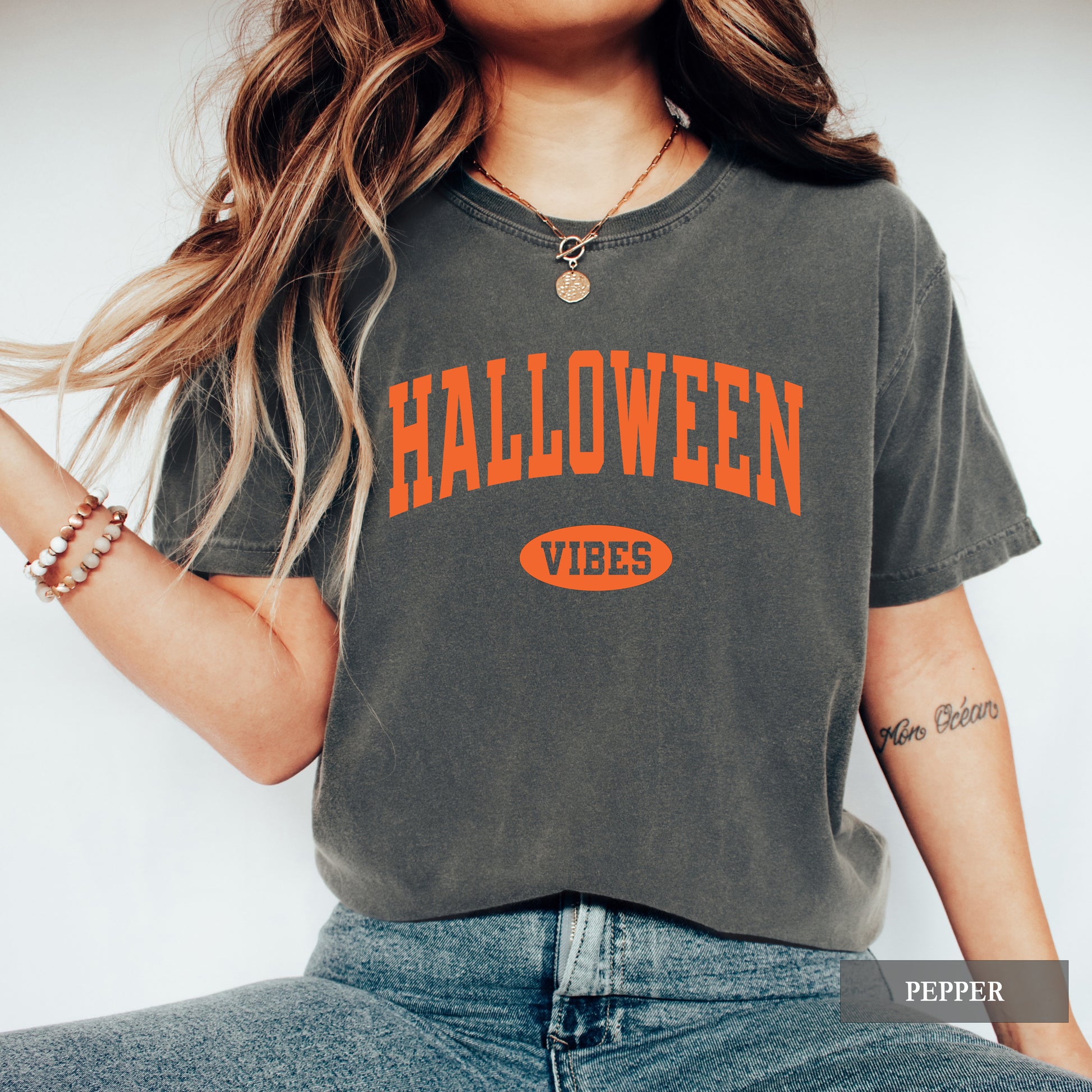 A woman wearing a pepper comfort colors tee with Halloween Vibes on the front.