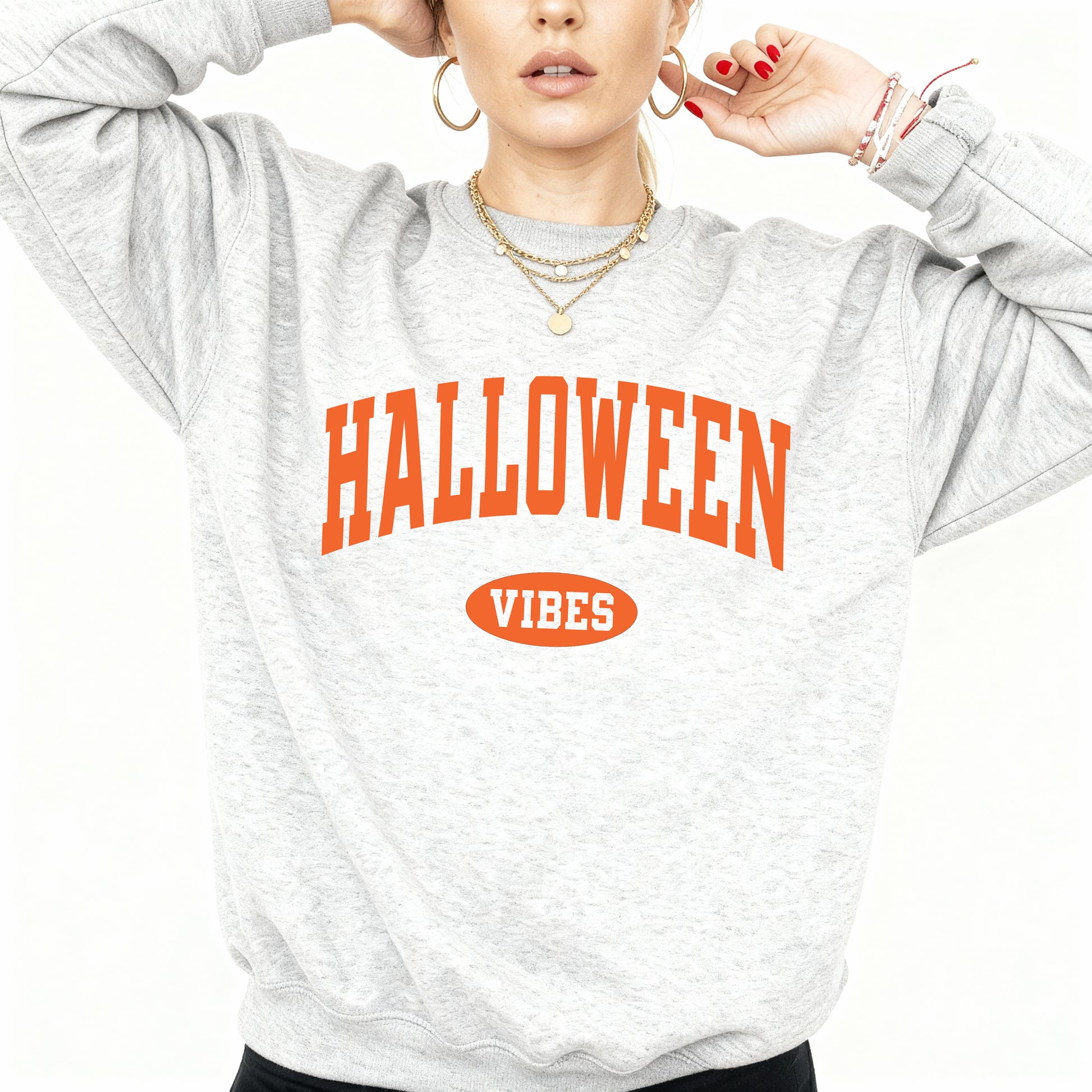 A woman wearing a light heather gray sweatshirt with 'HALLOWEEN VIBES' printed in orange on the front, posed against a plain white background.