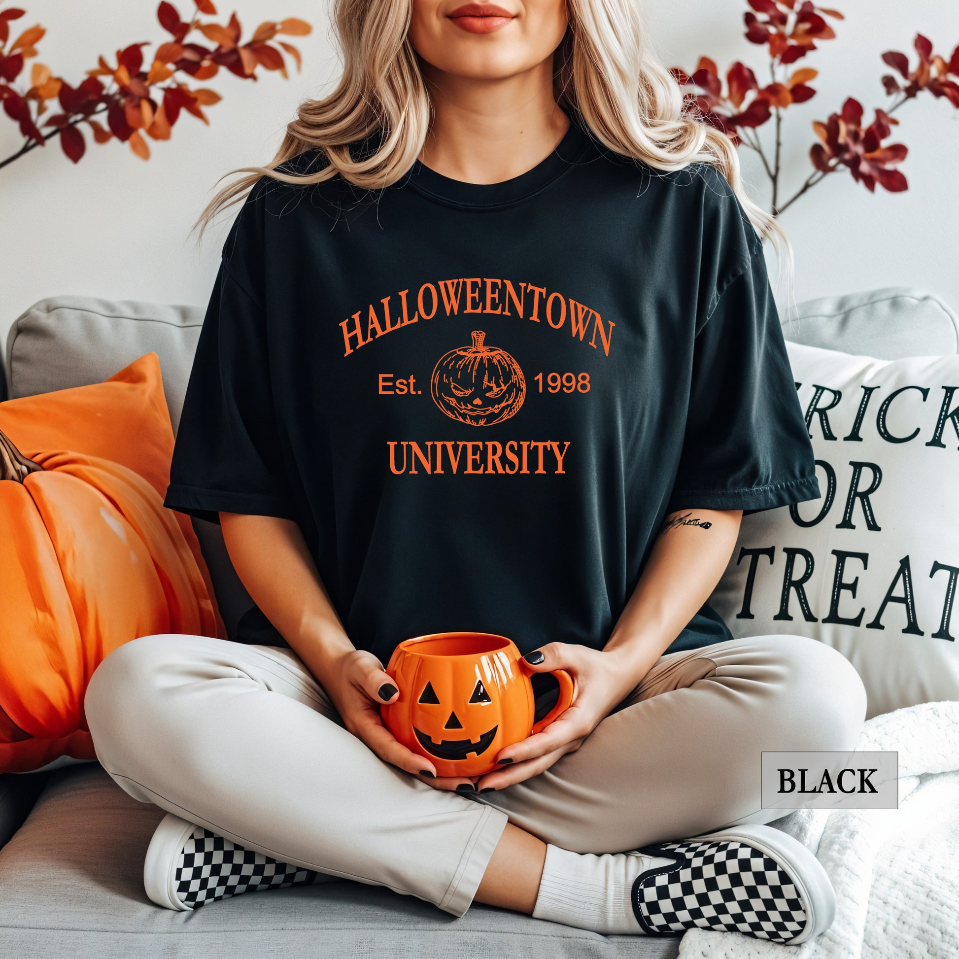Woman wearing a black comfort colors shirt that says Halloweentown University.