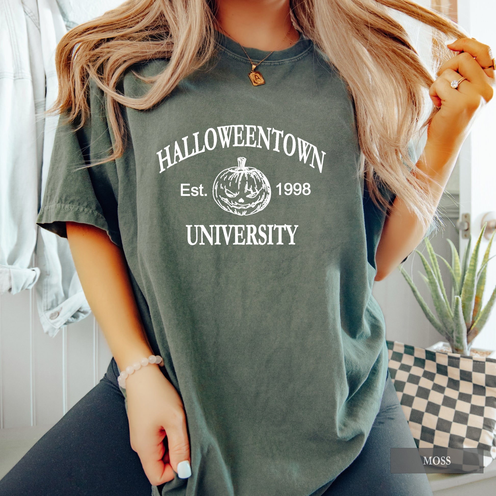Woman wearing a moss comfort colors shirt that says Halloweentown University.