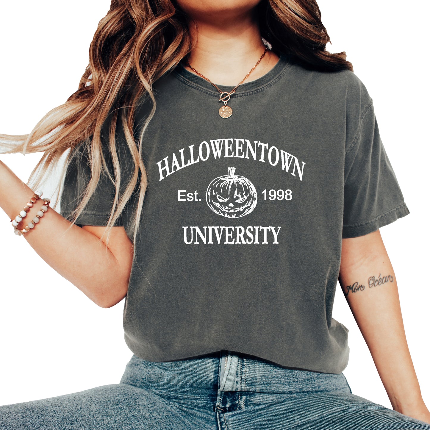 Woman wearing a pepper comfort colors shirt that says Halloweentown University.