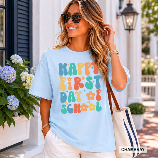 Woman wearing a light blue t-shirt with 'Happy First Day of School' text, standing outdoors.