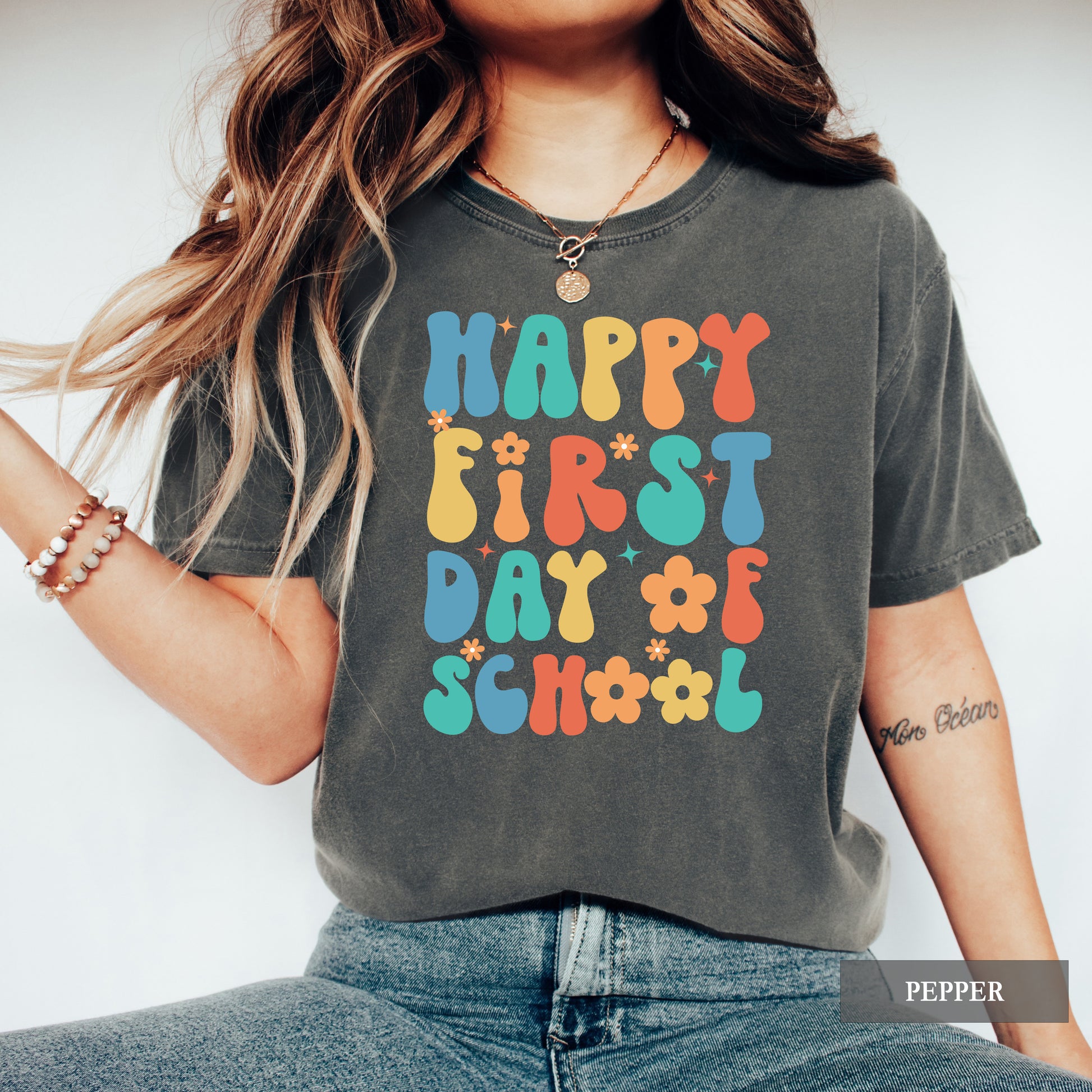 Person wearing a gray t-shirt with colorful 'Happy First Day of School' text.