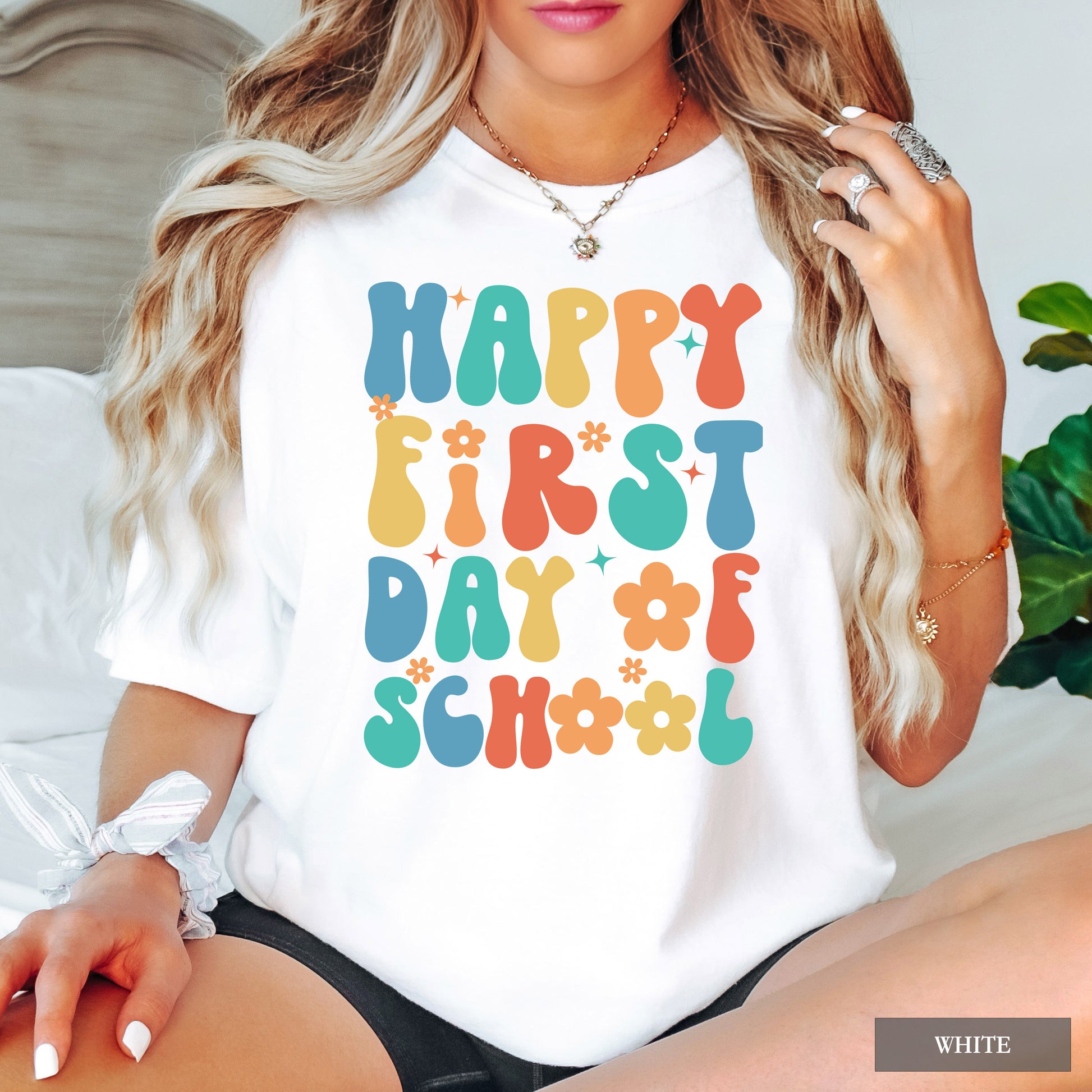 Person wearing a white t-shirt with colorful 'Happy First Day of School' text.
