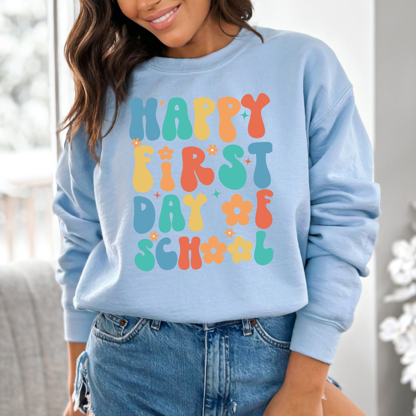 Person wearing a light blue sweatshirt with colorful 'Happy First Day of School' text.