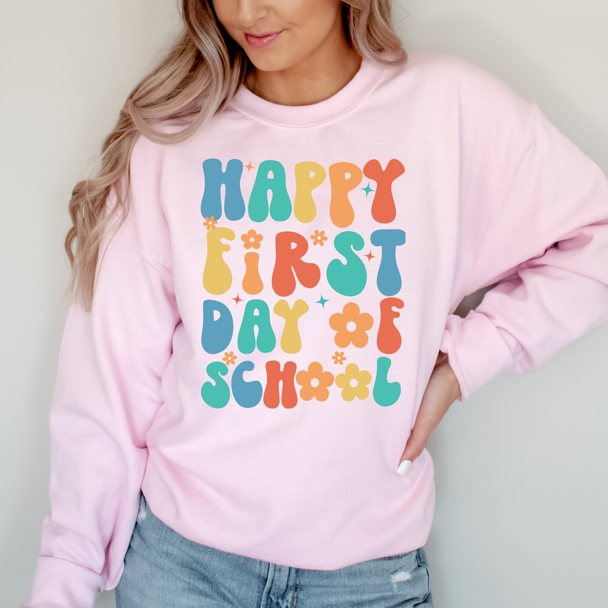 Person wearing a pink sweatshirt with 'Happy First Day of School' text in colorful letters.