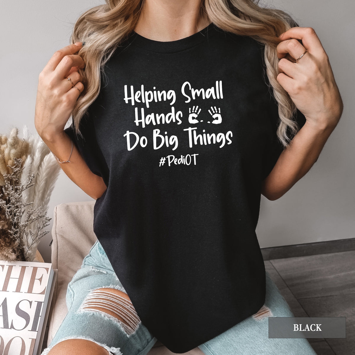 A woman wearing a black comfort colors shirt that says Helping Small Hands Do Big Things #PediOT