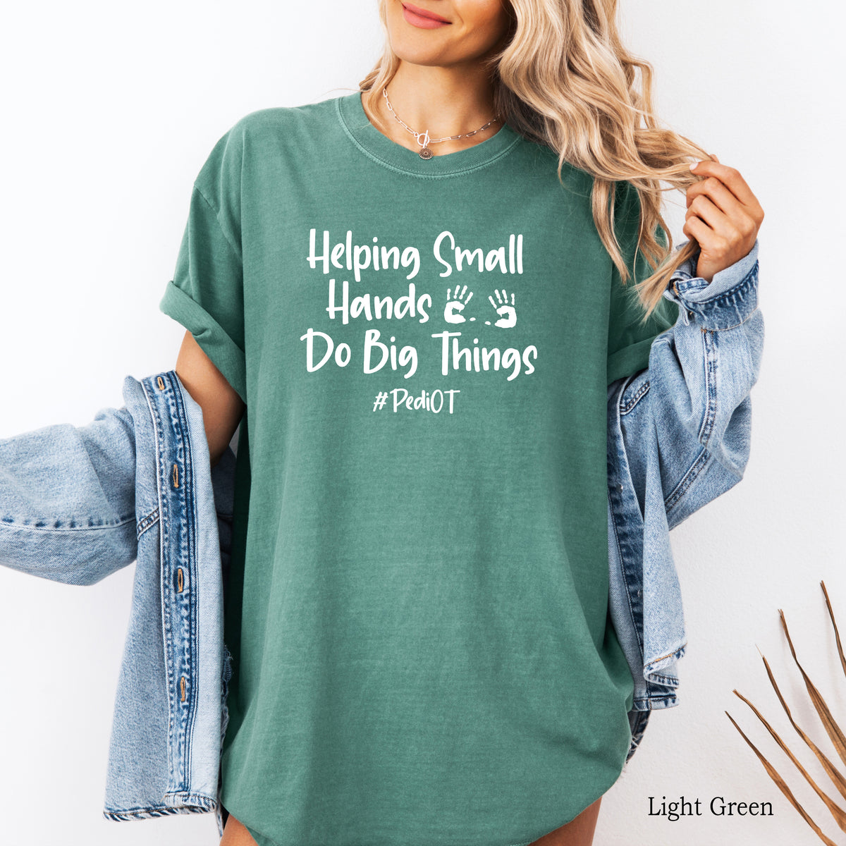 A woman wearing a light green comfort colors shirt that says Helping Small Hands Do Big Things #PediOT