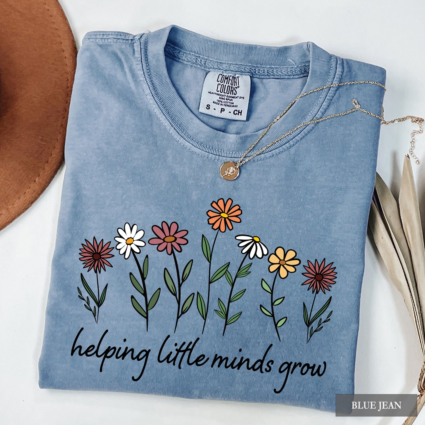 Folded blue denim shirt with floral design and text 'helping little minds grow' on a white background.