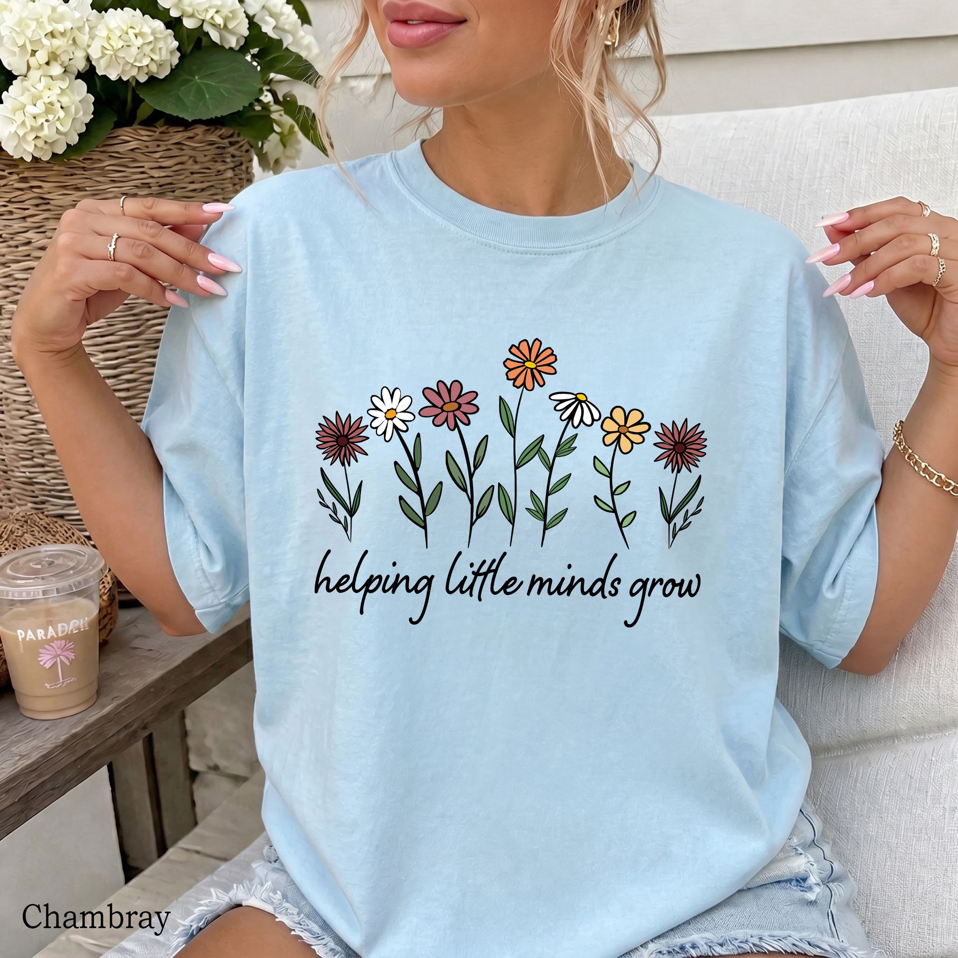 Person wearing a light blue t-shirt with floral design and text, sitting outdoors.
