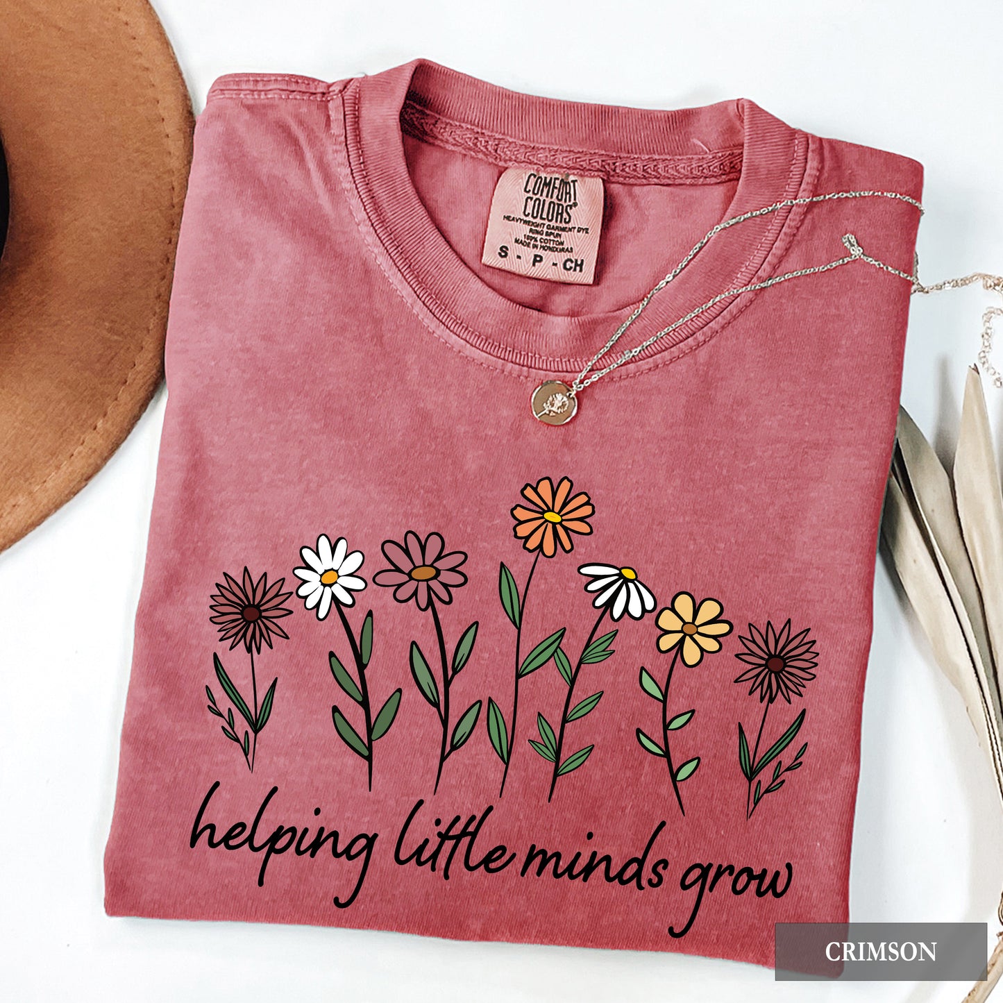 Folded pink shirt with floral design and text 'helping little minds grow' on a white background.