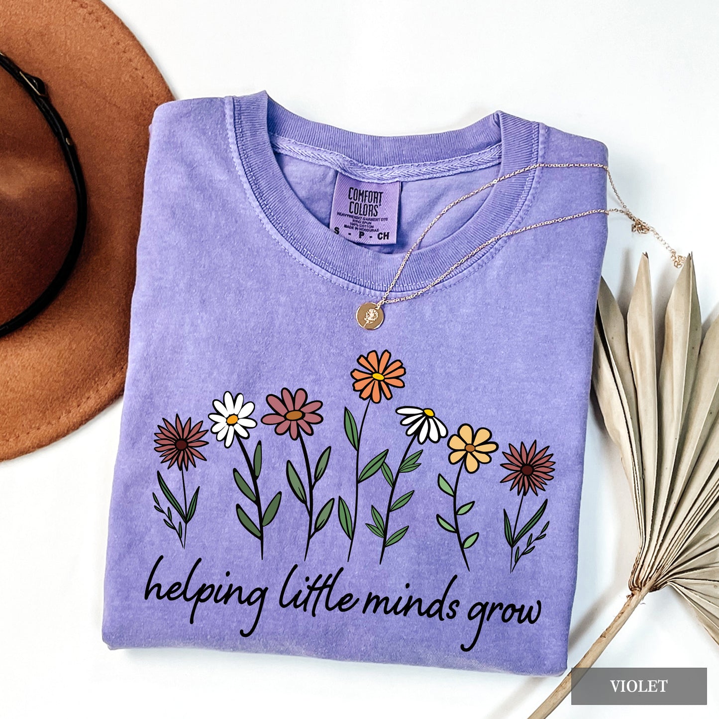 Folded purple shirt with floral design and text 'helping little minds grow' on a white background.