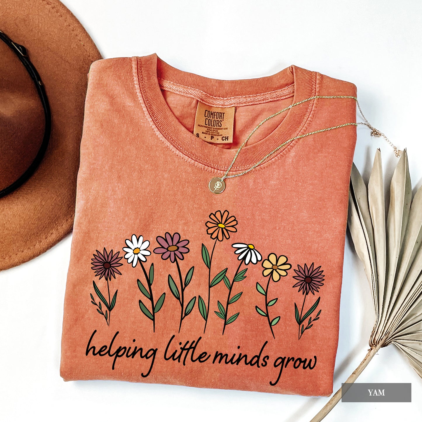 Folded peach-colored shirt with floral design and text 'helping little minds grow' on a white background.
