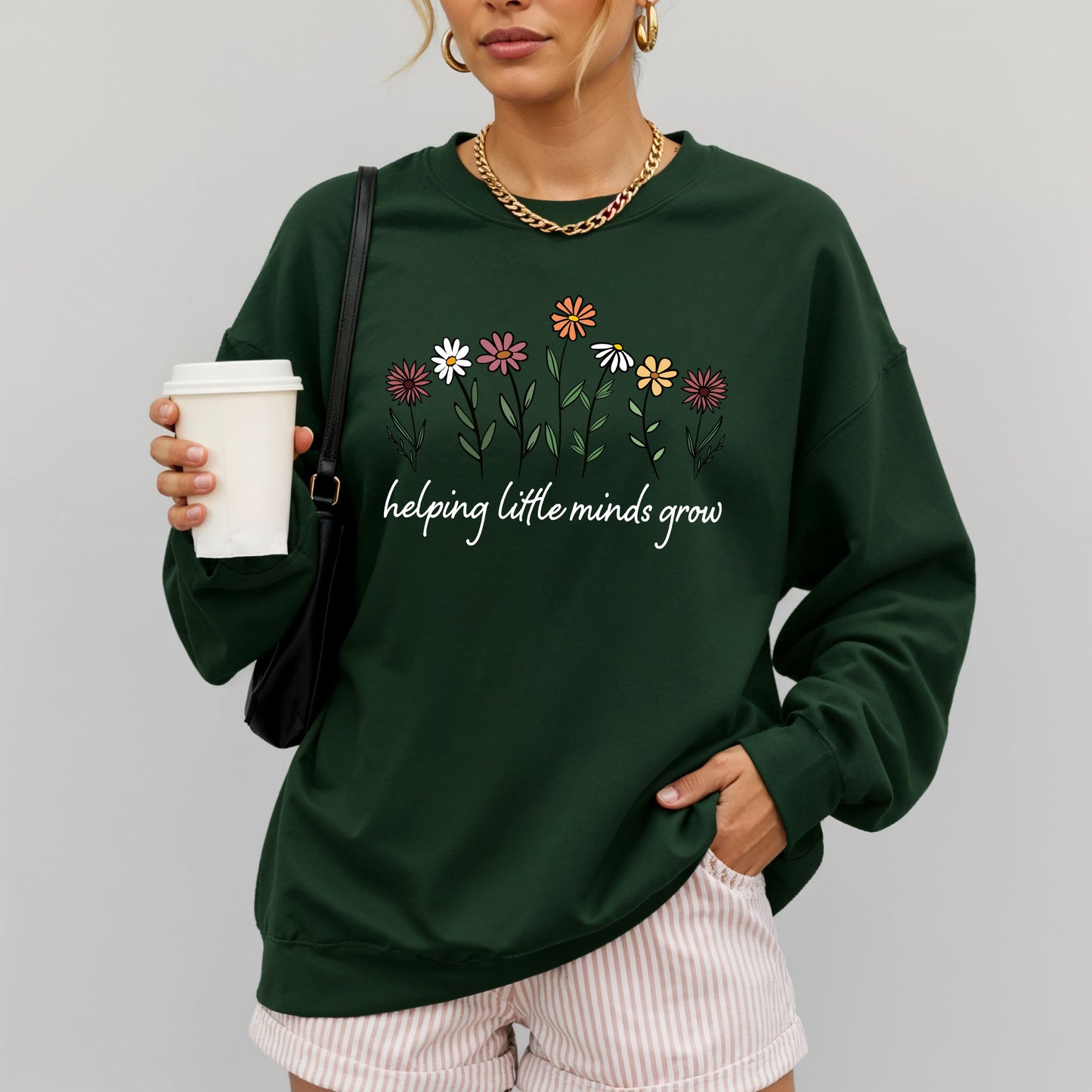 Person wearing a green sweatshirt with floral design and text, holding a coffee cup.