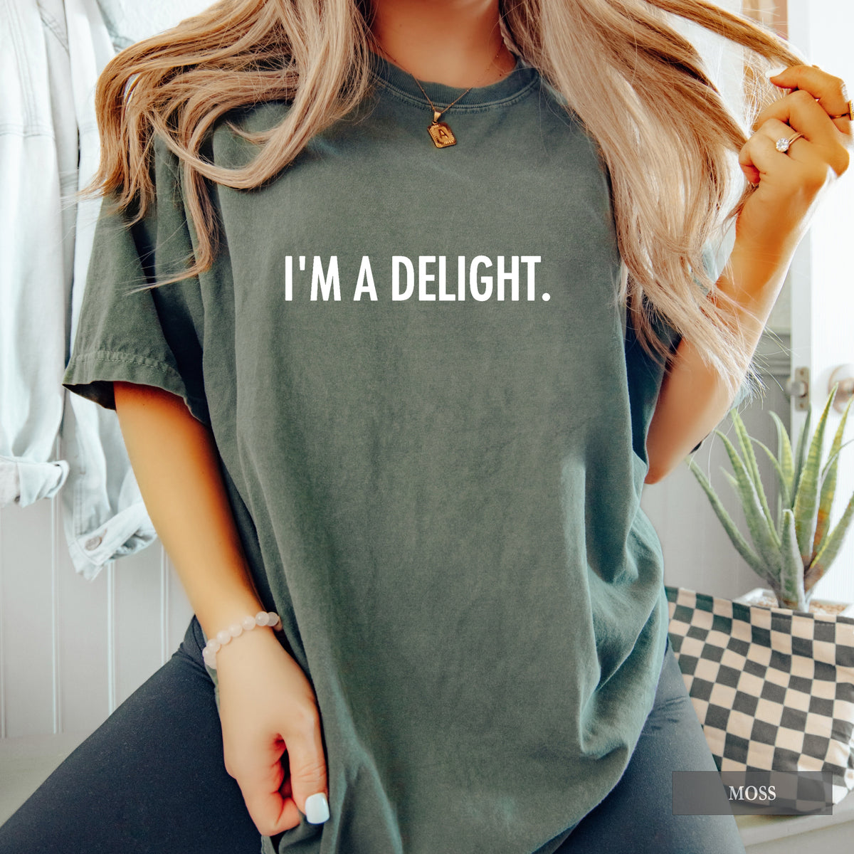A woman wearing a moss comfort colors shirt with 'I'm a Delight' on it in white print.