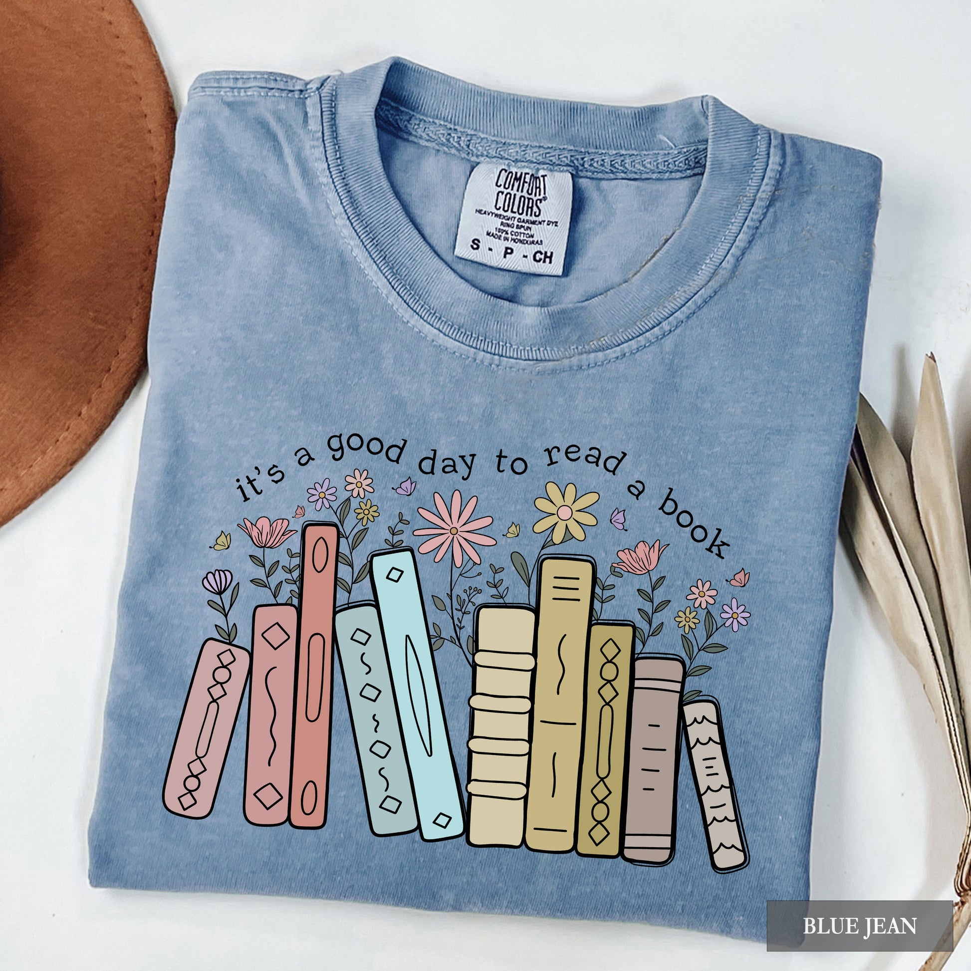 Folded blue shirt with book and flower design and text 'it's a good day to read a book' on a white background.