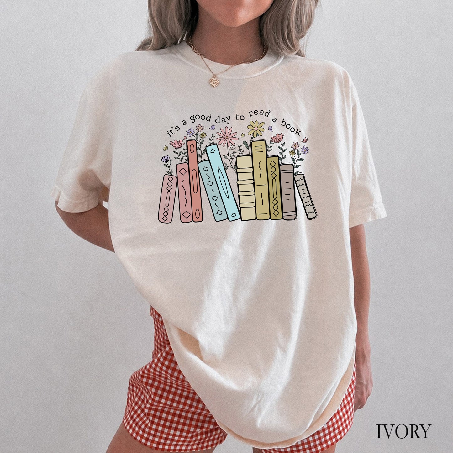 Person wearing a white t-shirt with colorful book design and text, standing against a plain background.