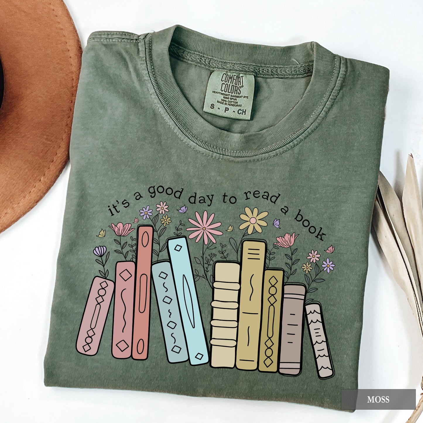 Folded green t-shirt with book and flower design and text 'it's a good day to read a book' on a white background.
