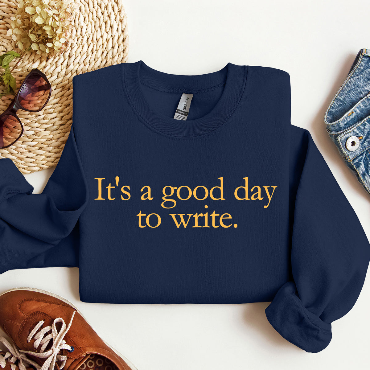 A navy blue crewneck sweatshirt with the phrase 'It's a good day to write.' printed in gold serif text across the chest.
