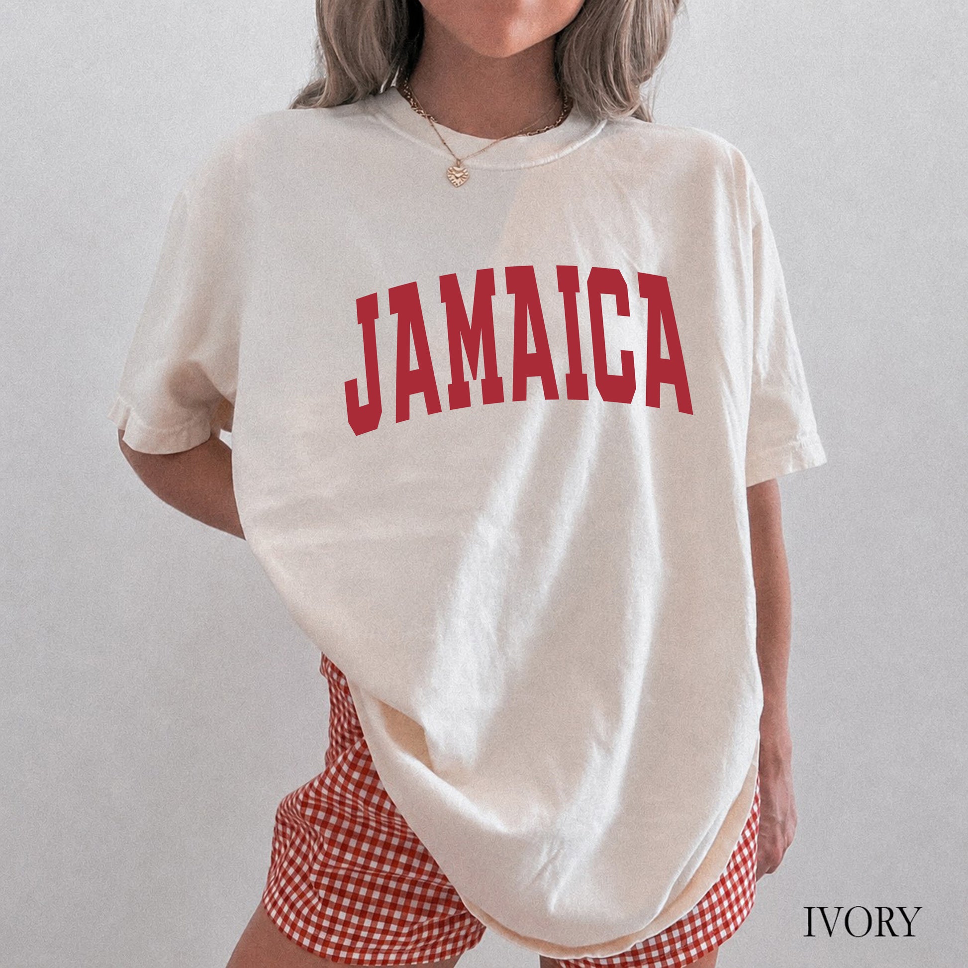 A woman wearing an oversized cream-colored t-shirt with 'JAMAICA' printed in red arched letters across the chest, paired with red and white gingham shorts. The image has a text overlay 'IVORY' in the bottom right corner.