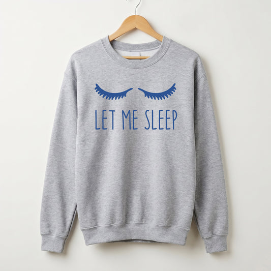 A light heather gray crewneck sweatshirt hanging on a wooden hanger against a plain off-white wall. The sweatshirt features a graphic of closed blue eyelashes above the text 'LET ME SLEEP' in blue.