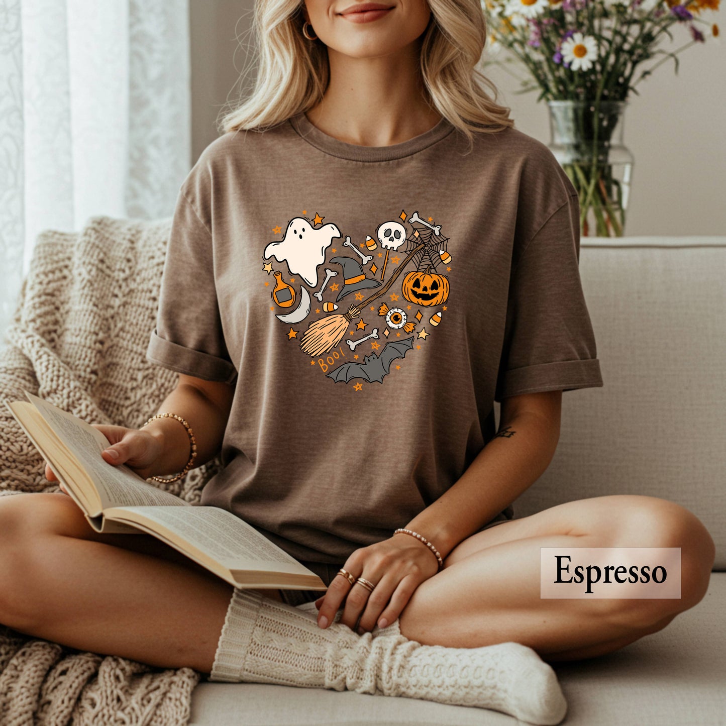 Woman wearing a brown t-shirt with Halloween-themed design, sitting on a couch holding a book.