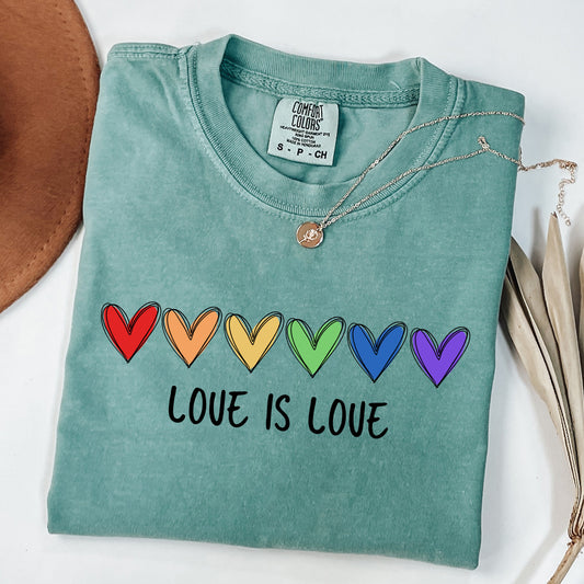 Folded teal t-shirt with rainbow hearts and 'Love is Love' text on a white background