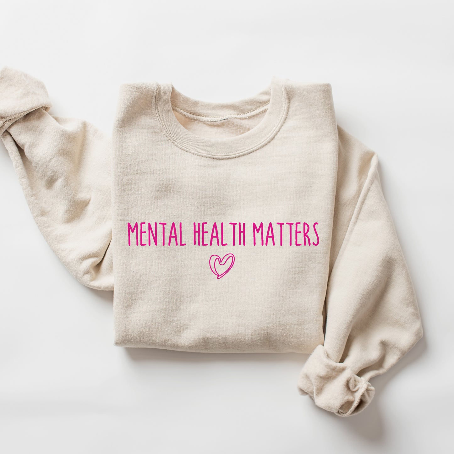 A folded cream-colored sweatshirt with the words 'MENTAL HEALTH MATTERS' printed in bright pink across the chest, accompanied by a small pink heart outline below, displayed on a clean white background.