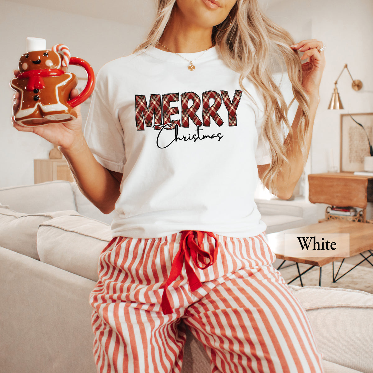 A woman wearing a white Comfort Colors shirt with Merry in red, green and cream plaid and Christmas underneath it.