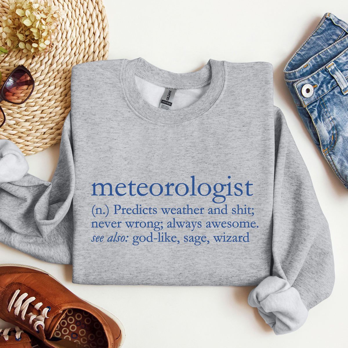 A grey crewneck sweatshirt that says 'meteorologist (n.) Predicts weather and shit; never wrong; always awesome. see also: god-like, sage, wizard
