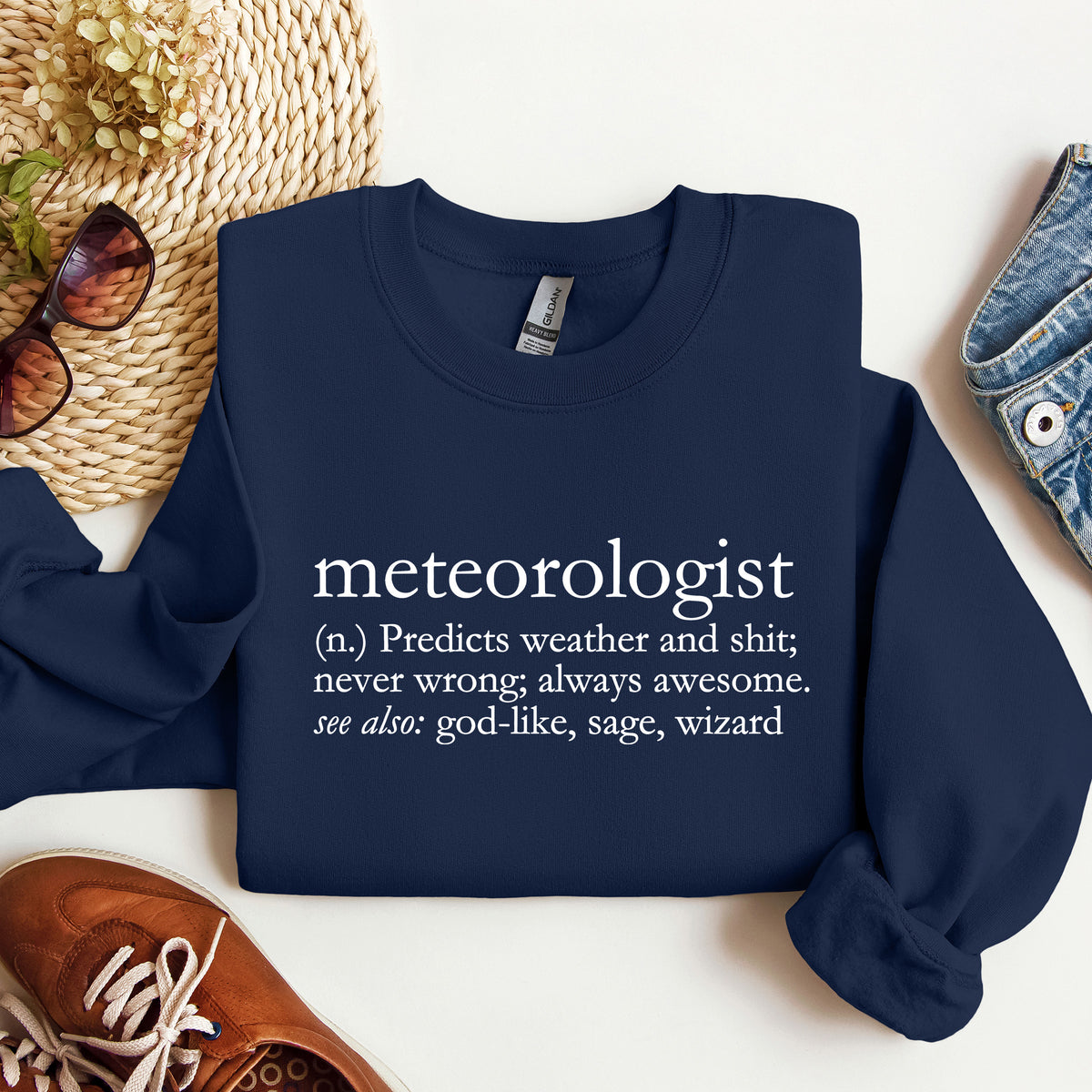 A navy crewneck sweatshirt that says 'meteorologist (n.) Predicts weather and shit; never wrong; always awesome. see also: god-like, sage, wizard