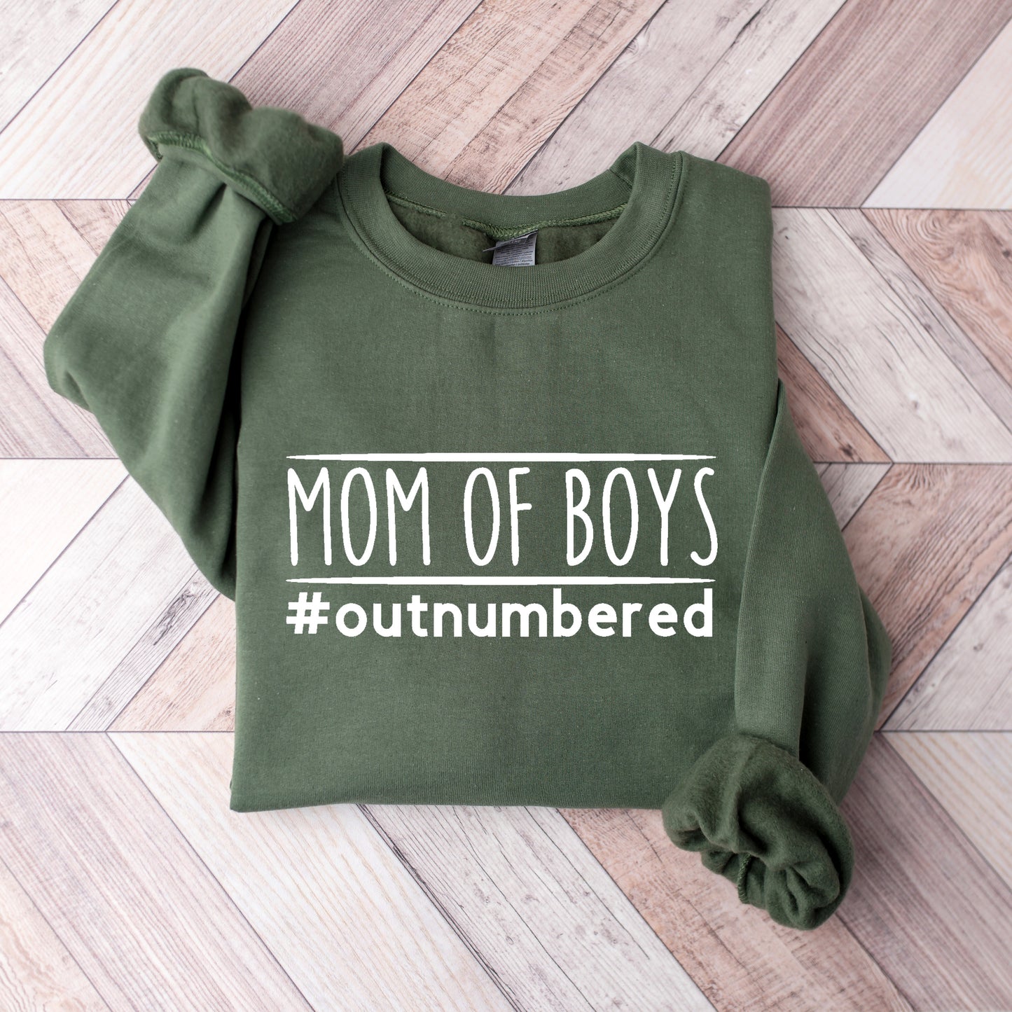Green sweatshirt with 'Mom of Boys #outnumbered' text on a wooden surface