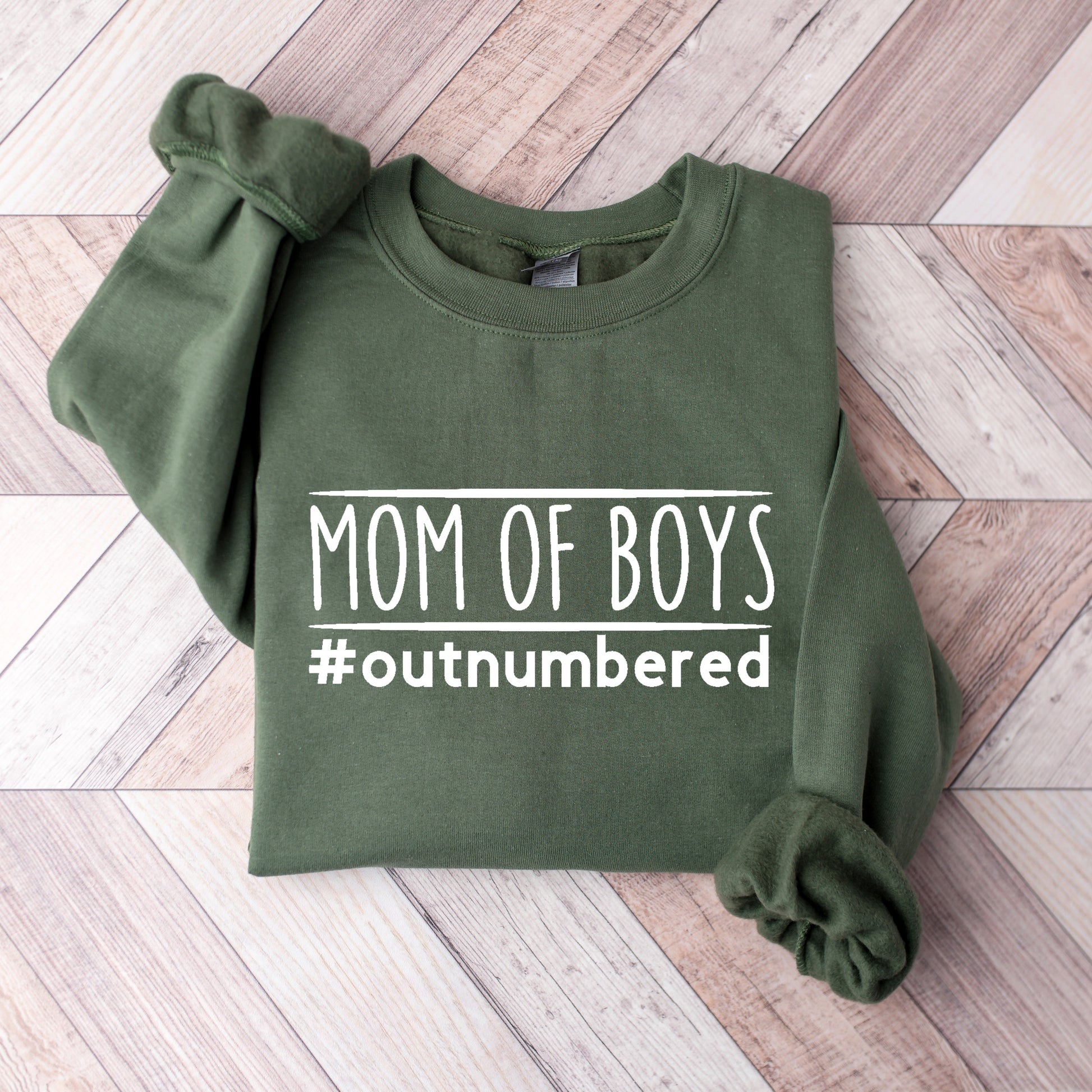 Green sweatshirt with 'Mom of Boys #outnumbered' text on a wooden surface