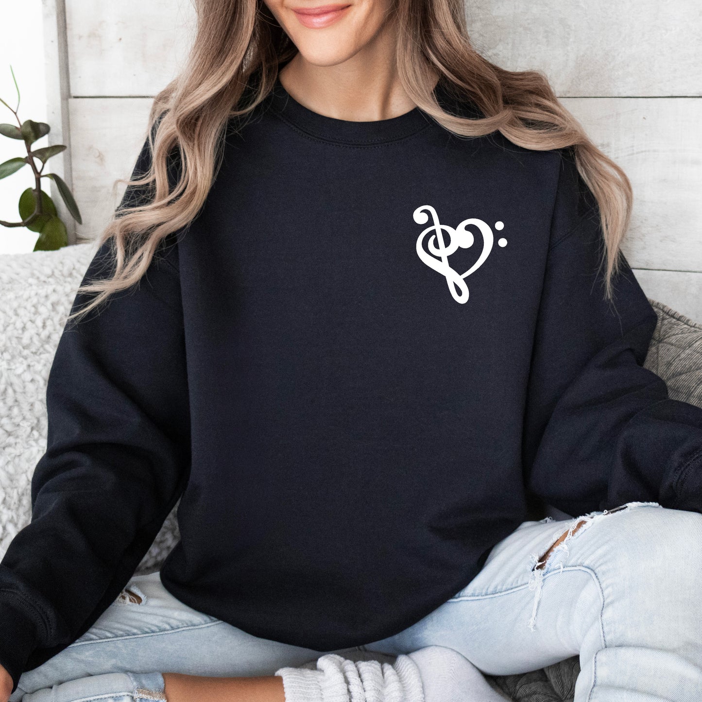 A woman wearing a black gildan sweatshirt with a musical note shaped like a heart on the pocket area.
