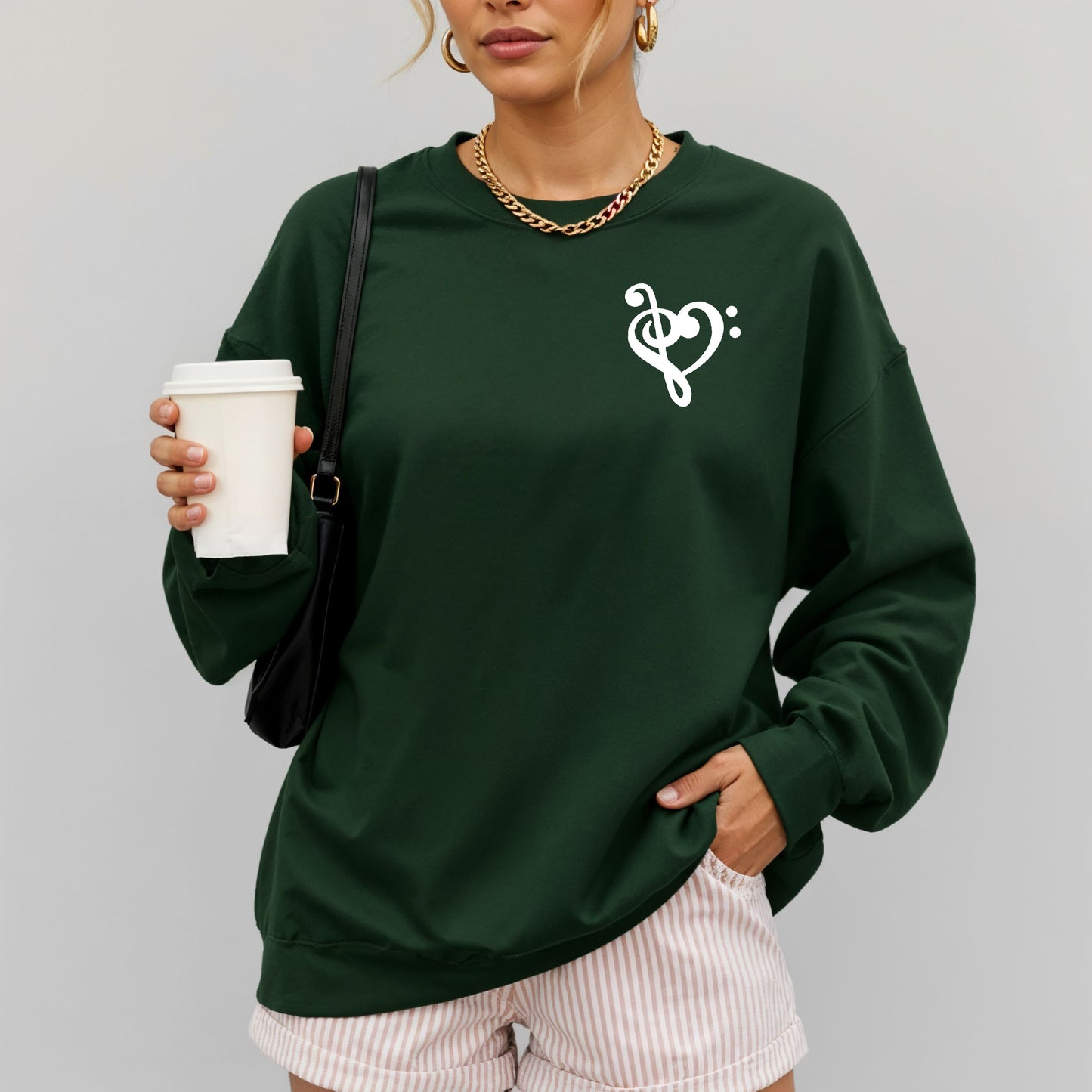 A woman wearing a dark green gildan sweatshirt with a musical note shaped like a heart on the pocket area.

