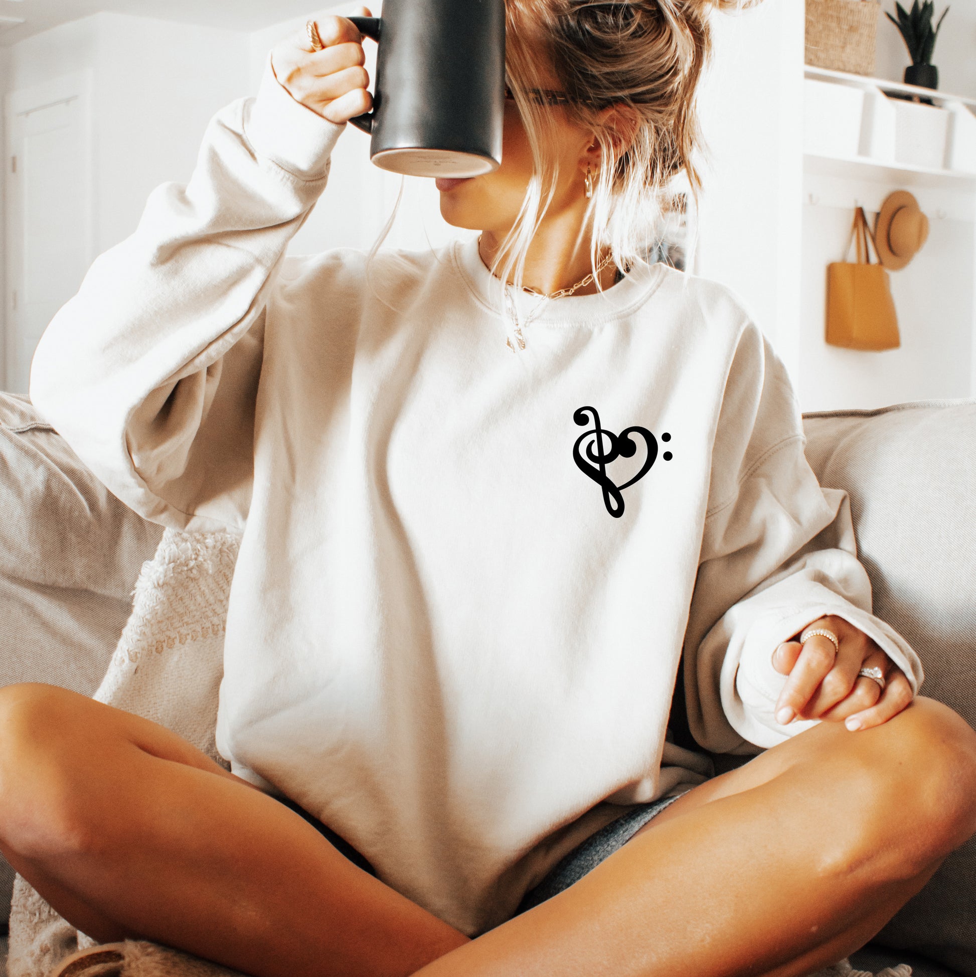 A woman wearing a sand gildan sweatshirt with a musical note shaped like a heart on the pocket area.
