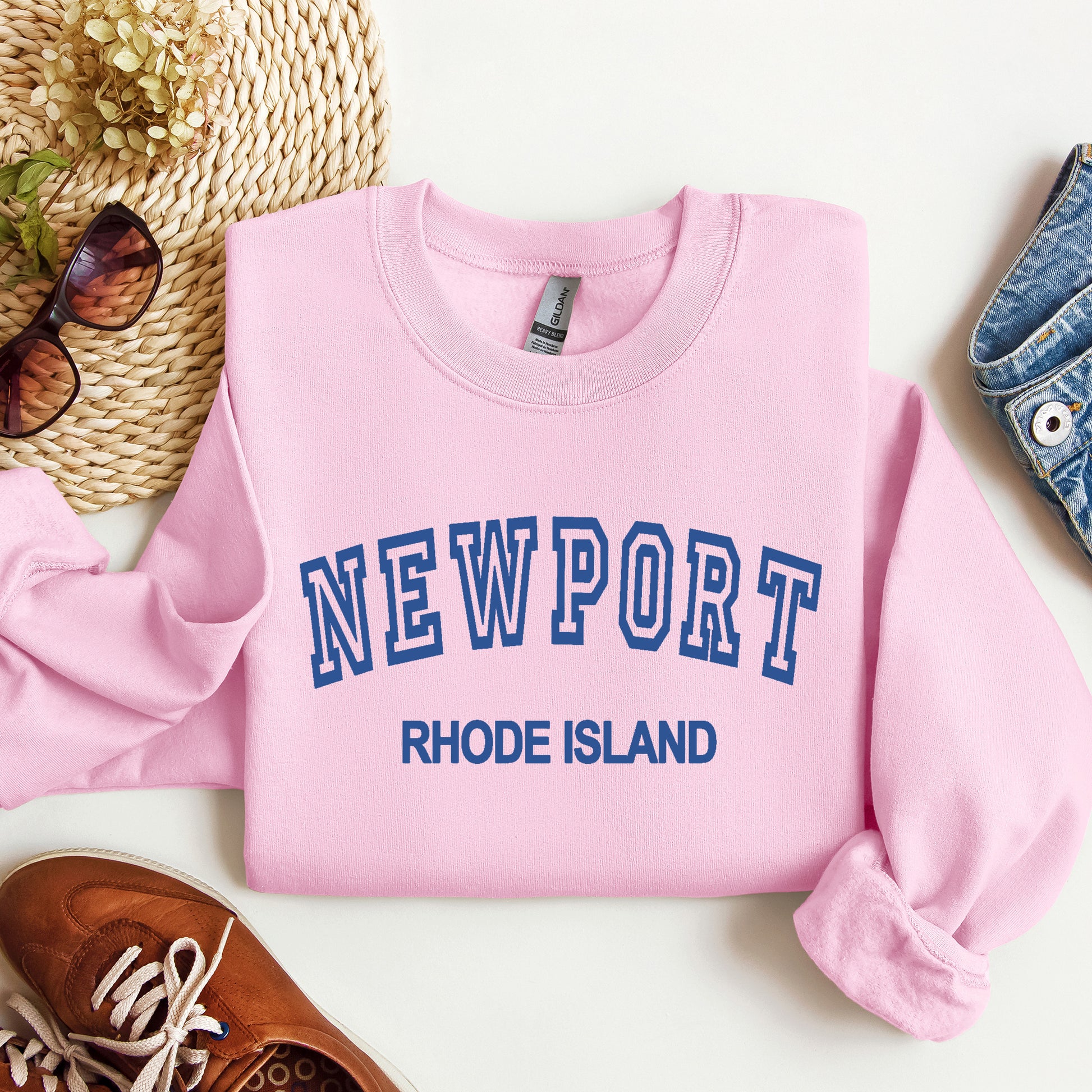 Pink sweatshirt with 'Newport Rhode Island' text on a white surface with accessories.