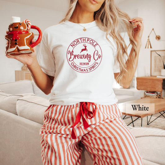 A woman wearing a white comfort colors shirt with 'North Pole Brewing Co' on it in red print.
