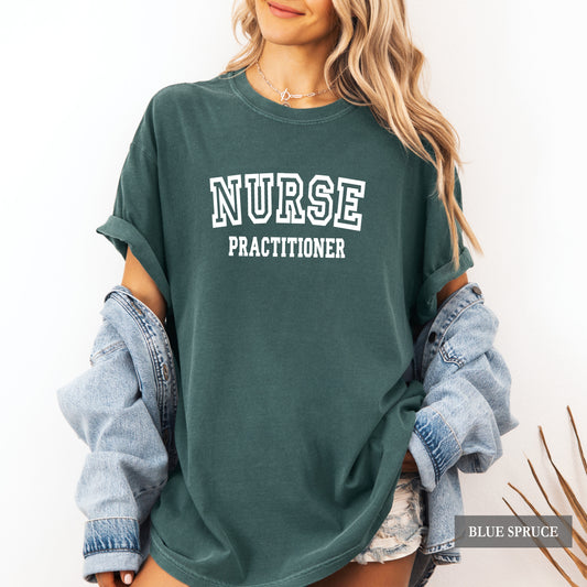 A woman wearing an oversized dark teal-green t-shirt with 'NURSE PRACTITIONER' printed in white block letters on the front, styled with rolled-up light-wash denim sleeves and denim shorts.