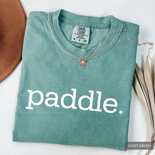 A folded light green t-shirt with the word 'paddle.' printed in white lowercase letters across the front.
