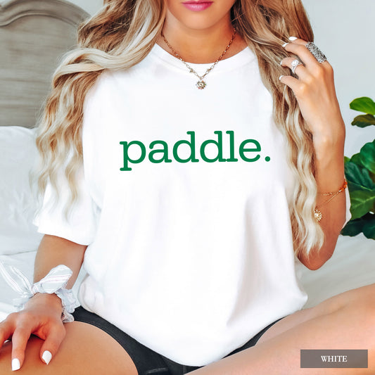 A woman wearing a white short-sleeve t-shirt with the word 'paddle.' printed in green lowercase letters across the chest.