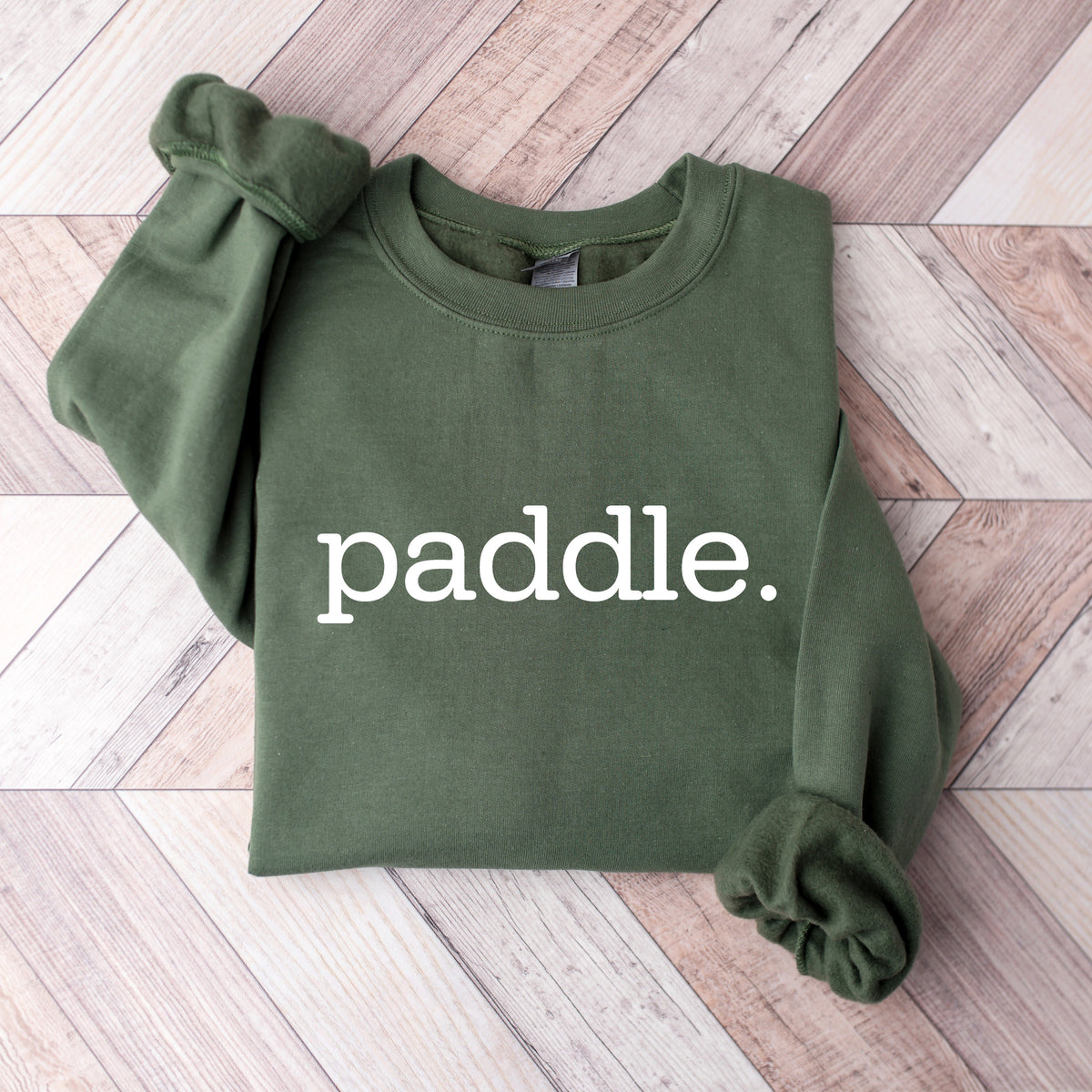 Green sweatshirt with the word 'paddle' on a wooden floor