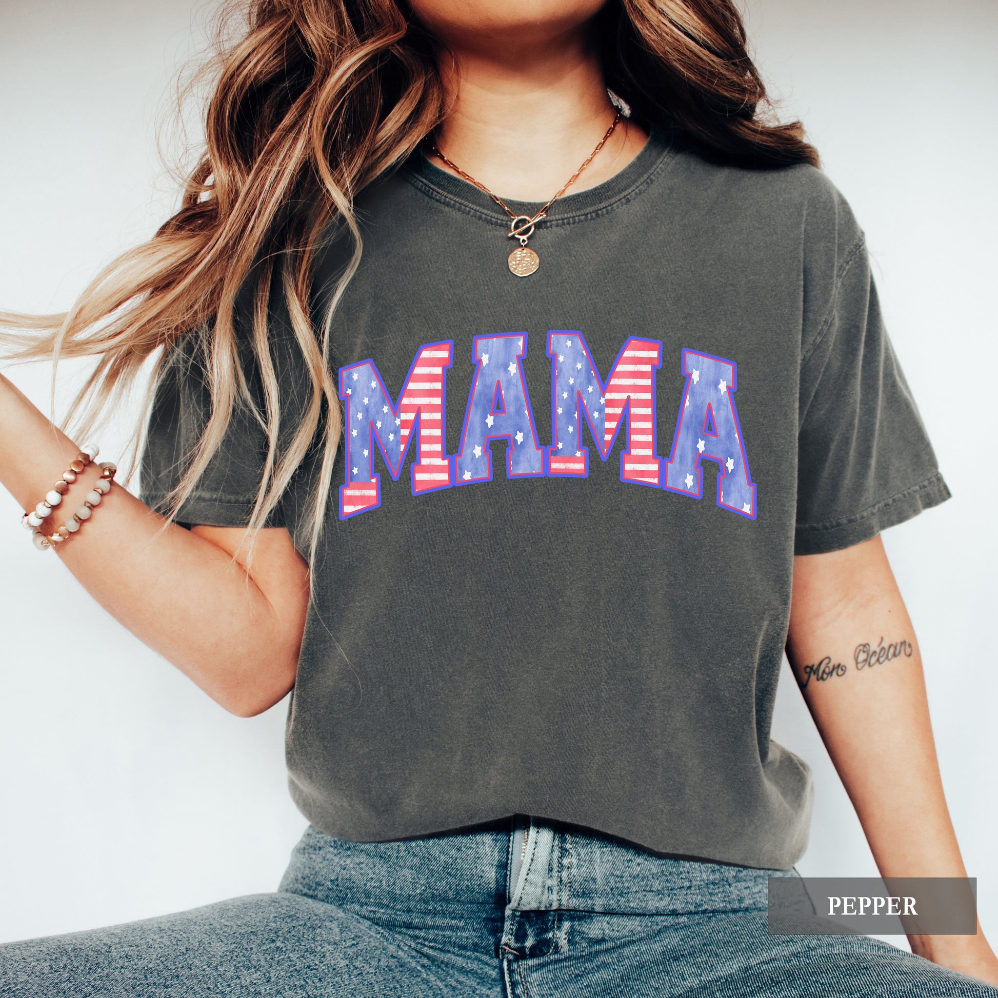 Person wearing a dark gray t-shirt with 'MAMA' printed in red white and blue american flag letters on a plain background.