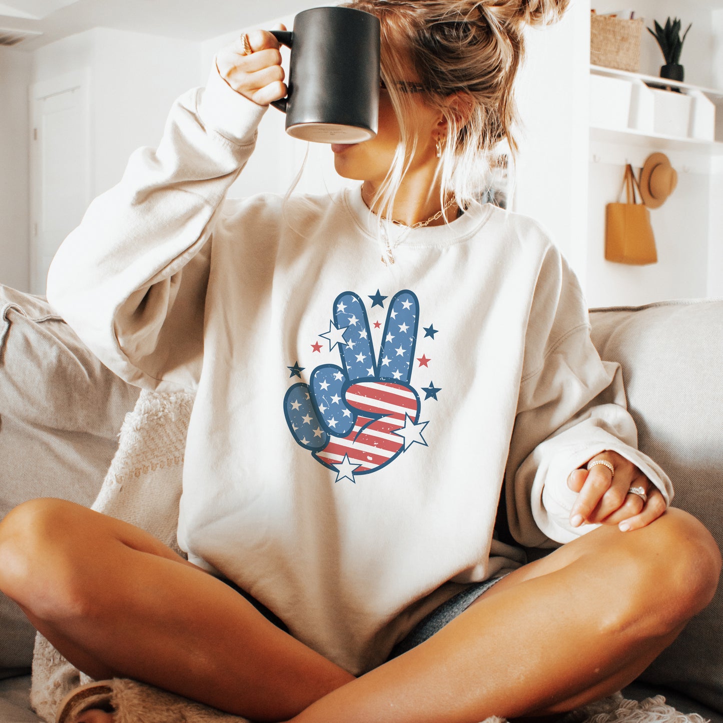 Person wearing a white sweatshirt with a peace sign design, sitting on a couch holding a mug.