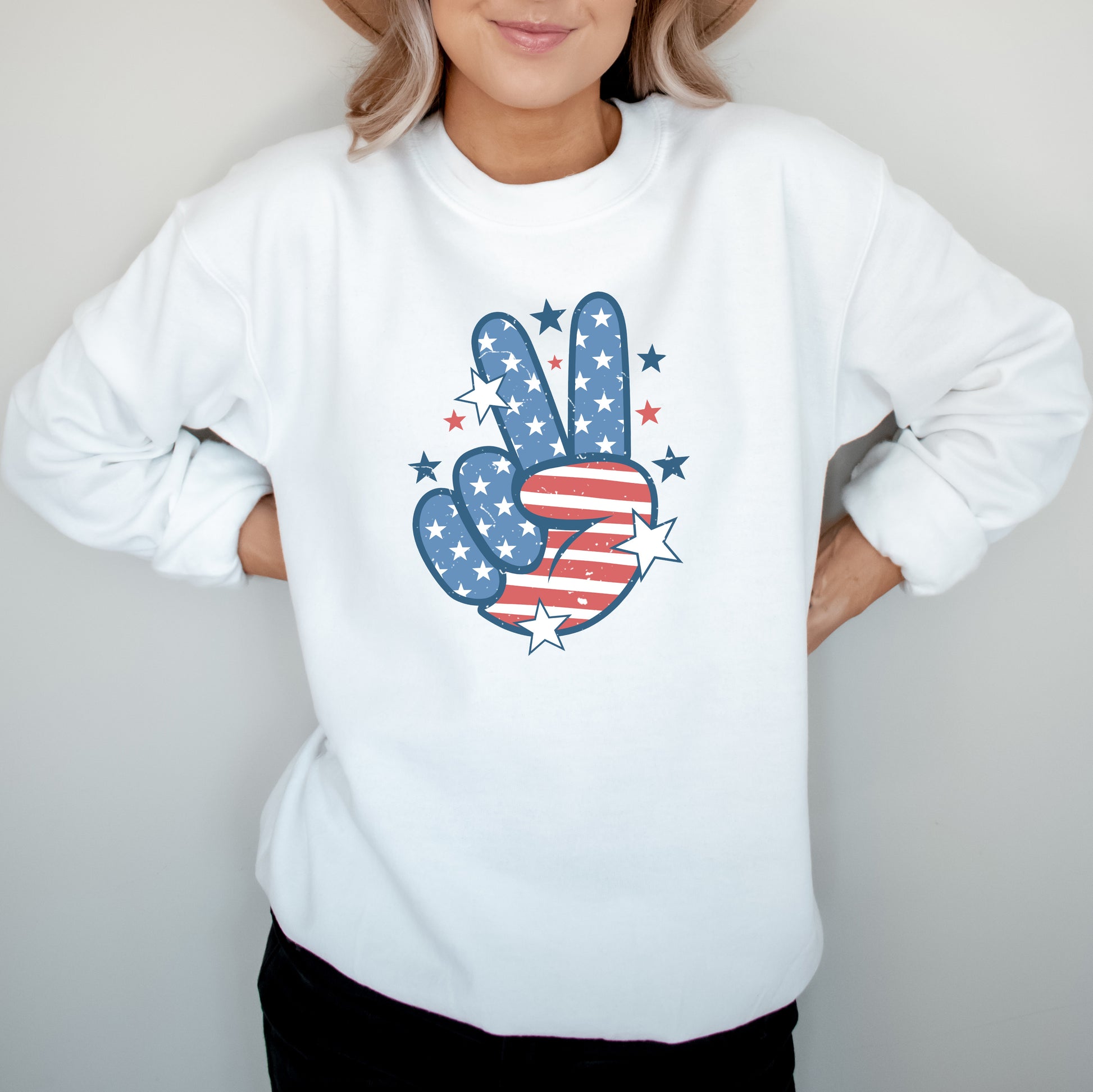 Person wearing a white sweatshirt with a peace sign design featuring American flag colors on a plain background