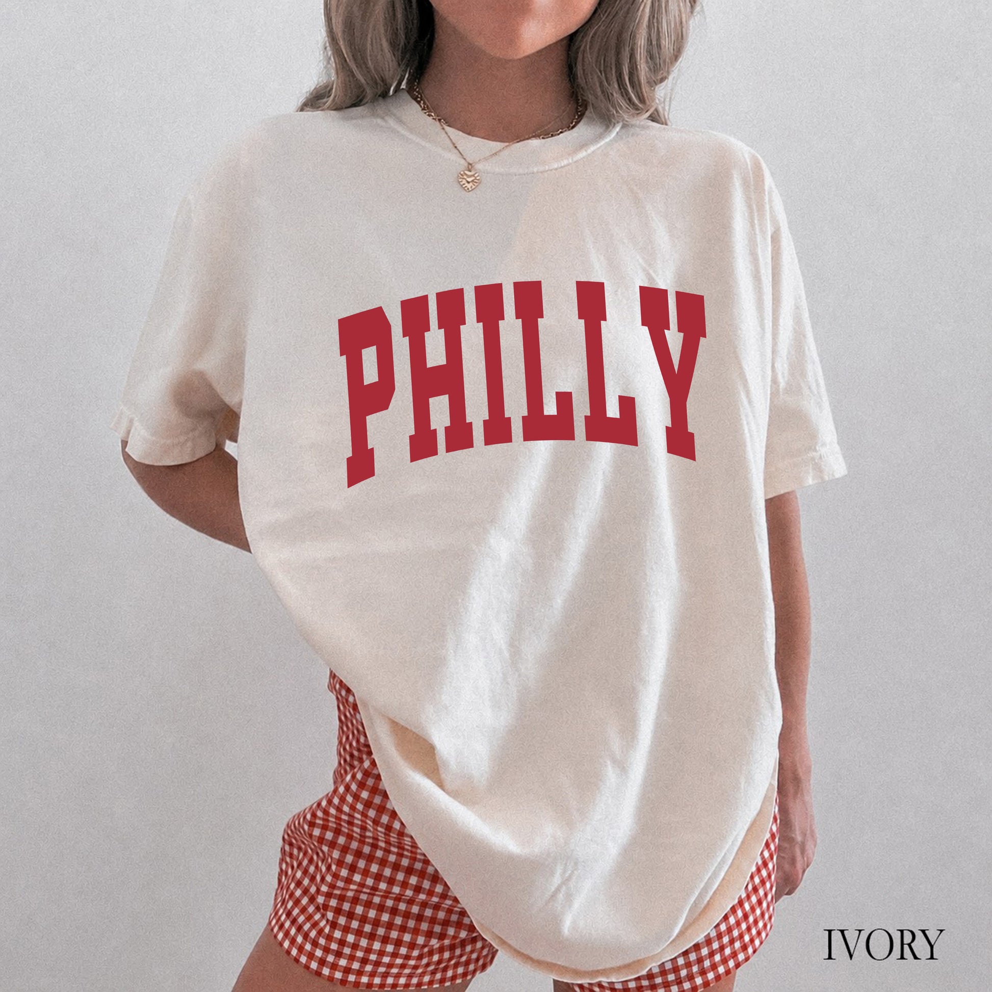 Woman wearing an ivory comfort colors t-shirt that says Philly on the front.